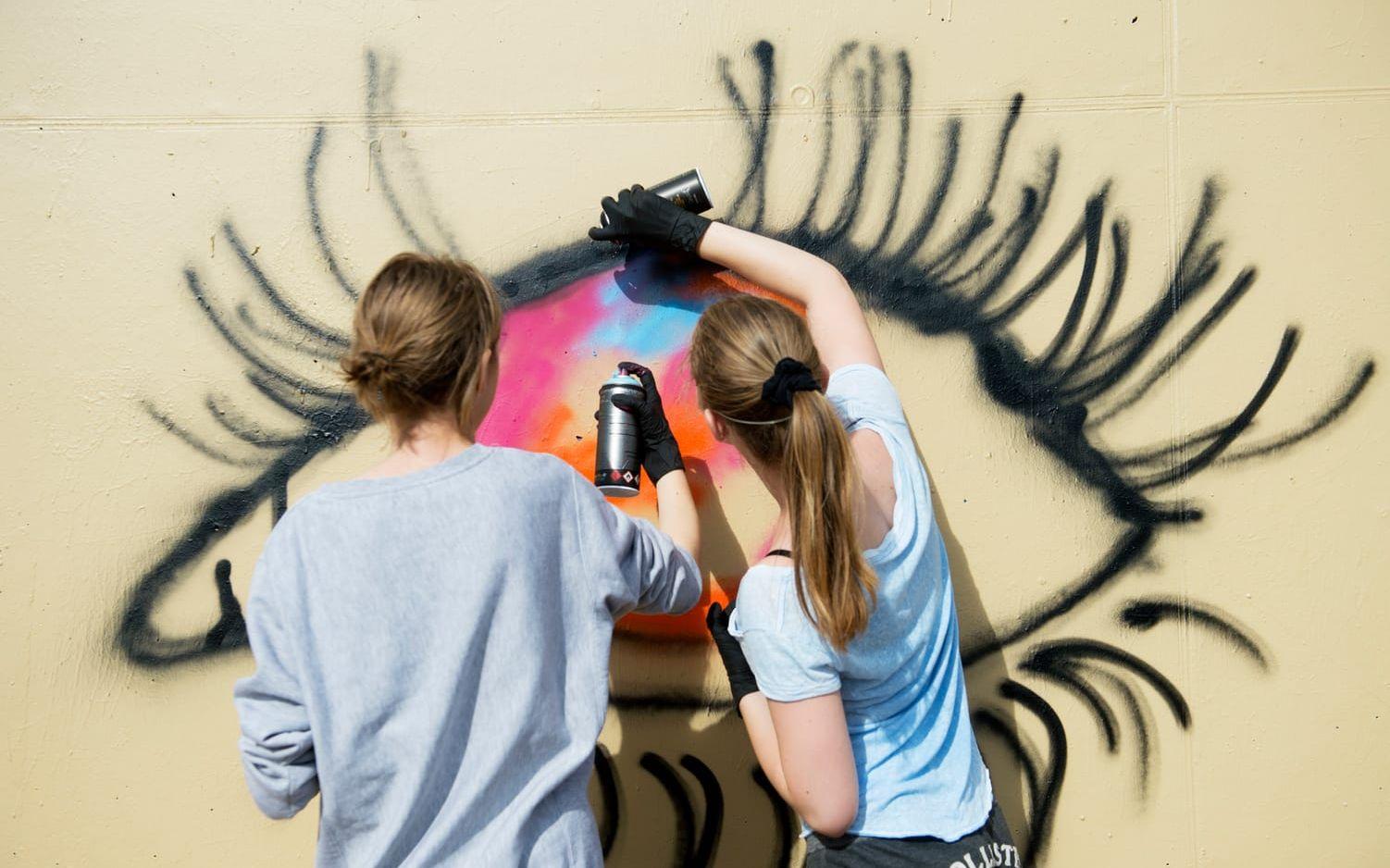 Lagarbete. Klasskompisarna Sandra Kis och Mila Jones från Sturegymnasiet hjälps åt att måla ögon på väggen. Till sist sprejar de ett feministtecken rakt över pupillen. Bild: Jari Välitalo