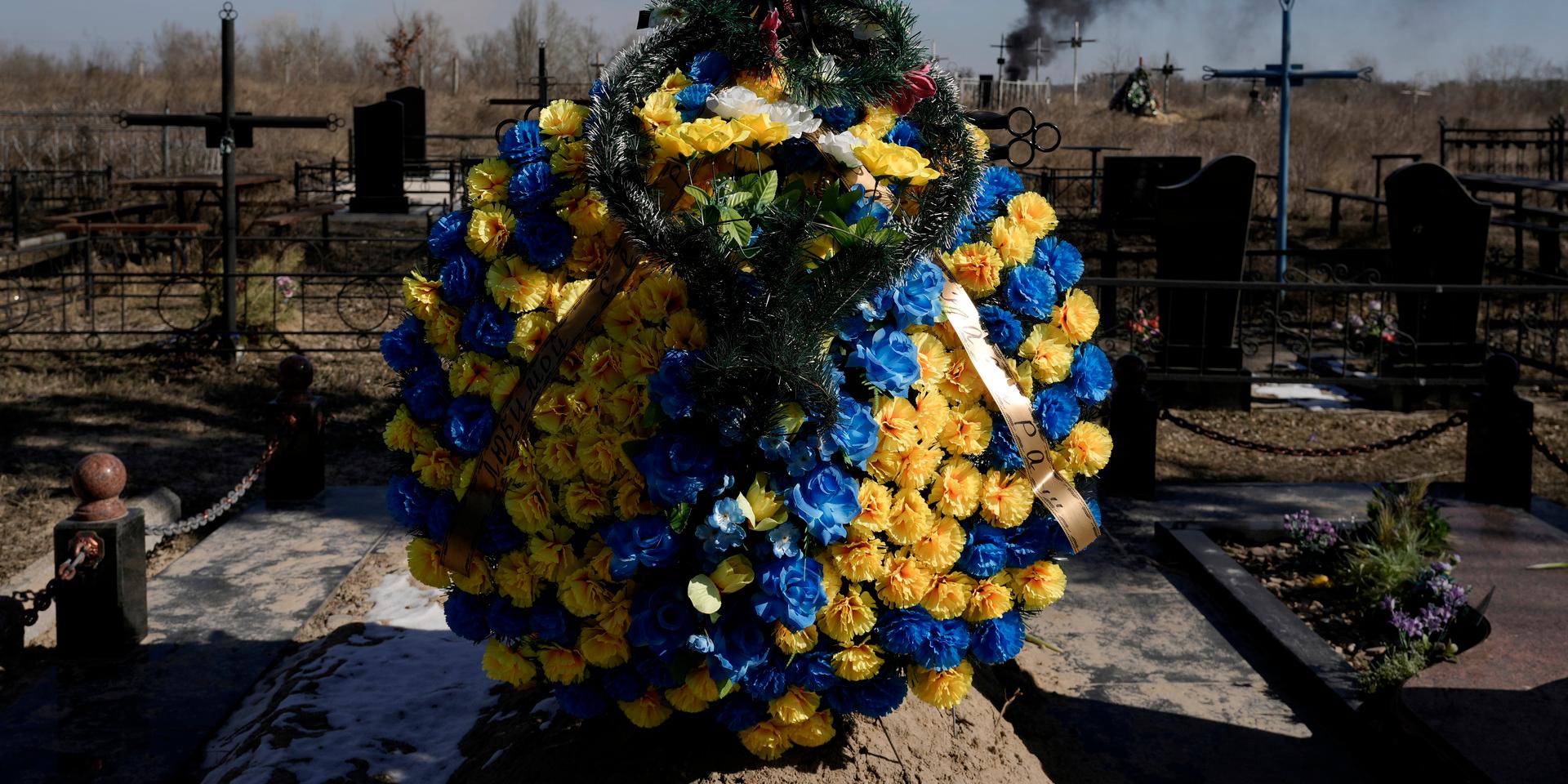 Motstånd. Blommor på en kyrkogård utanför Kiev, med rök från en artilleriattack i bakgrunden.