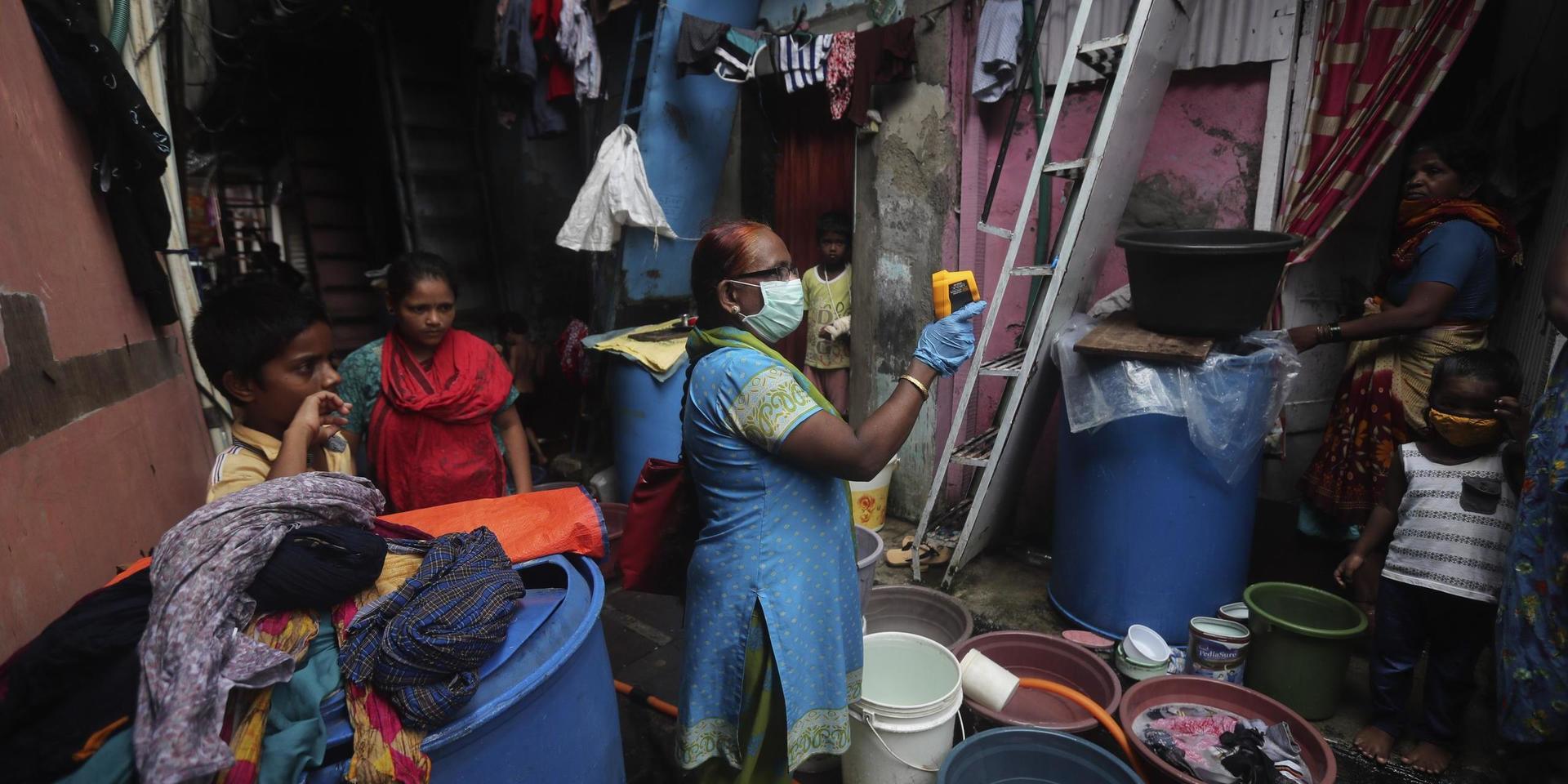 En sjukvårdsarbetare mäter kroppstemperaturen på invånare i Bombays slumområde Dharavi i Indiden. 