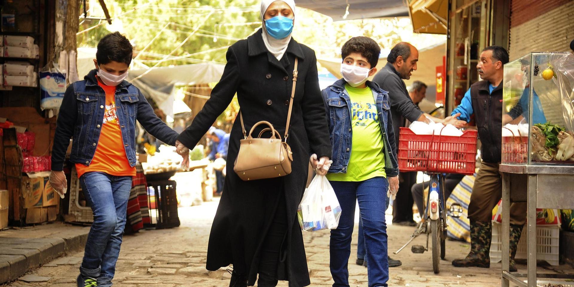 En syrisk kvinna och hennes två söner på en marknad i huvudstaden Damaskus – där munskydd blivit en allt vanligare syn. 
