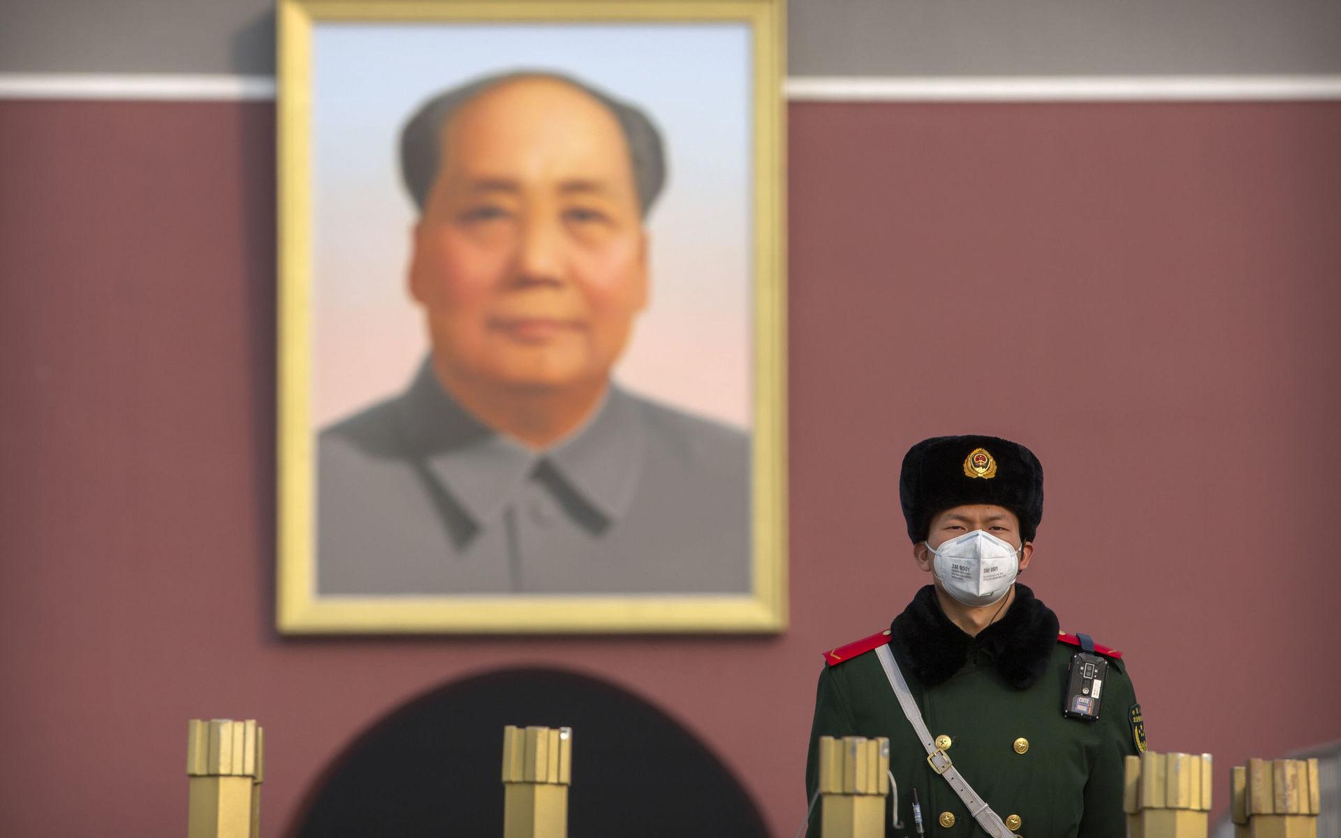 Nutid i Kina. En polisman med munskydd framför en bild av Mao Zedong.