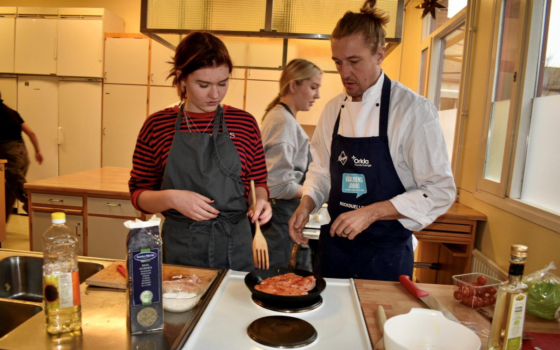 Sturegymnasiets restauranglärare Björn Berling ger Selma Abrahamsson och Moa Larsson tips på hur de kan tänka när det är dags att steka kycklingfilén.