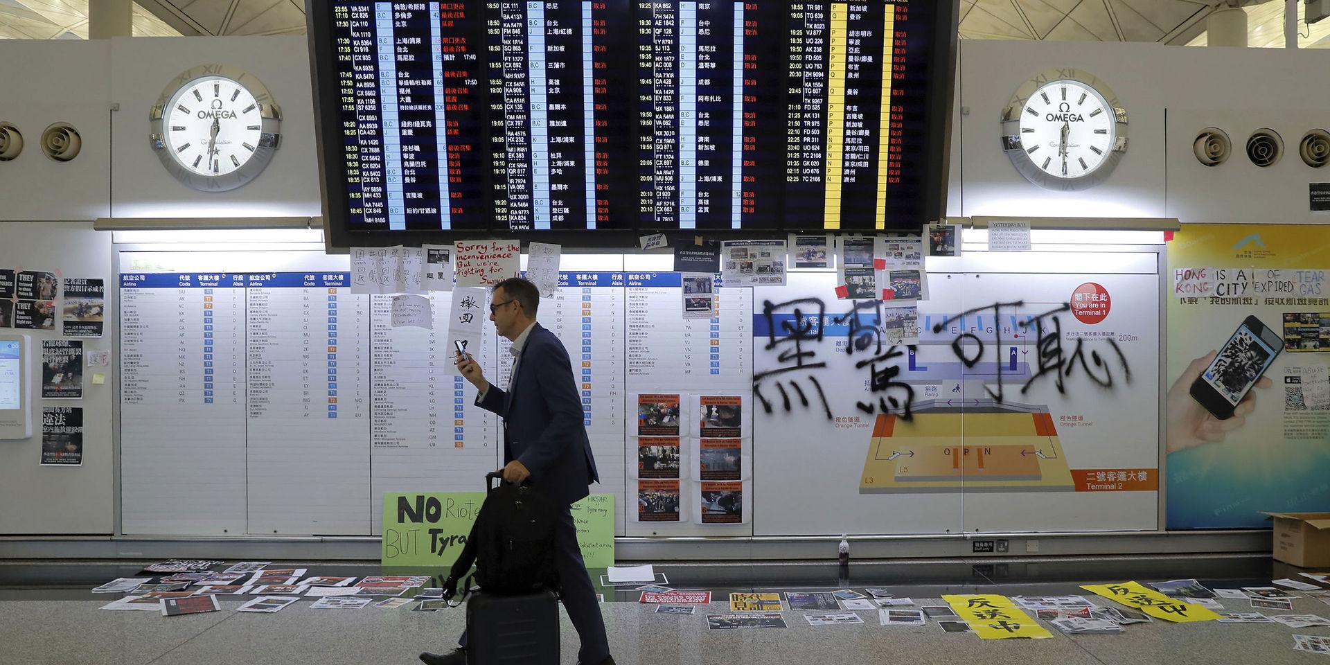A traveler walks by protest placards placed around the flights information board as thousands of protesters stage a sit-in protest at the Hong Kong International Airport, Monday, Aug. 12, 2019. One of the world&apos;s busiest airports canceled all flights after thousands of Hong Kong pro-democracy protesters crowded into the main terminal Monday afternoon. (AP Photo/Kin Cheung)