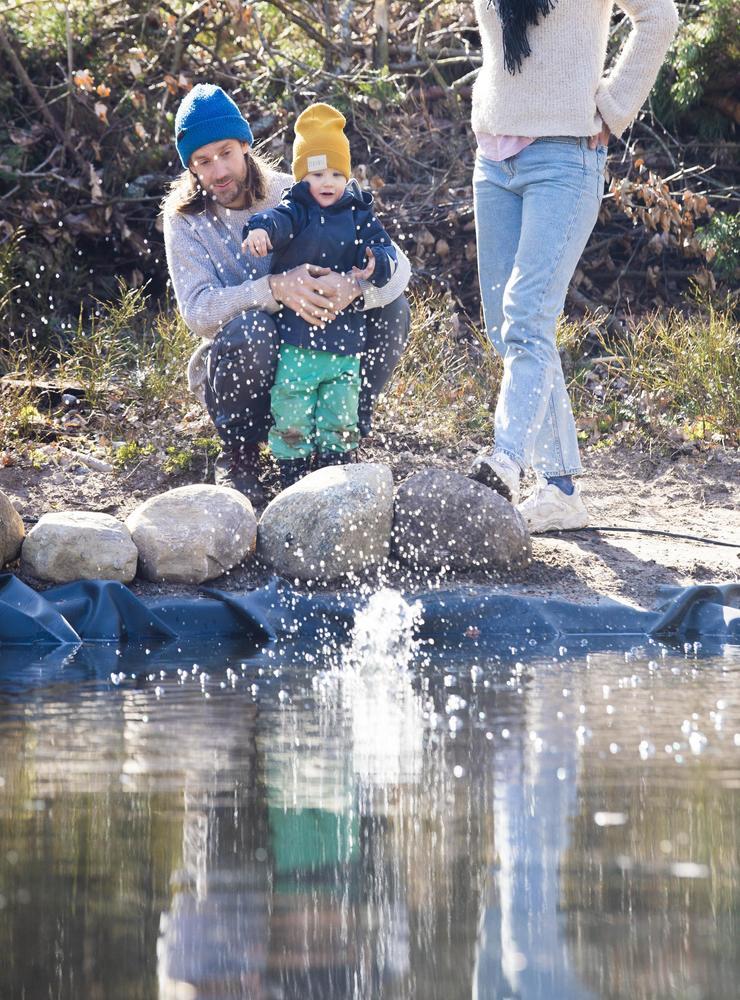 Sonen Vilgot, i pappa Kristian Jakobssons famn, tycker att det är en höjdare att kasta sten i poolen.