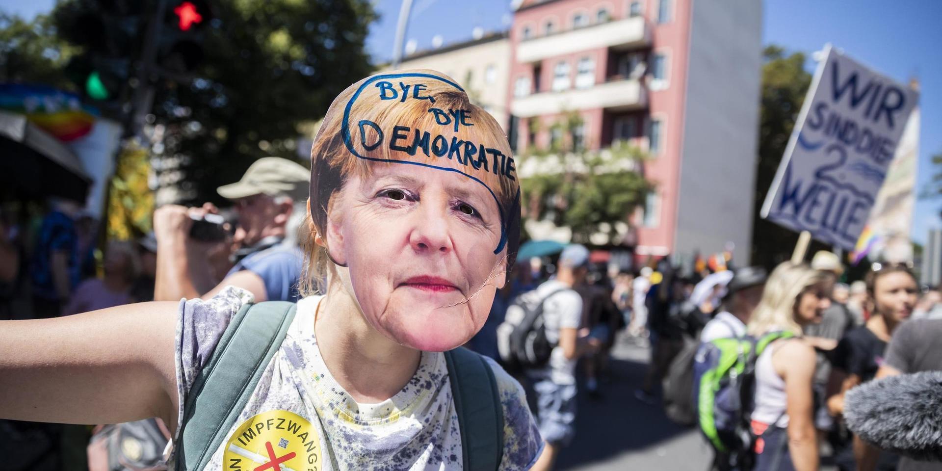 En demonstrant har skrivit orden 'hej då demokrati' på en mask föreställande den tyska förbundskanslern Angela Merkel.