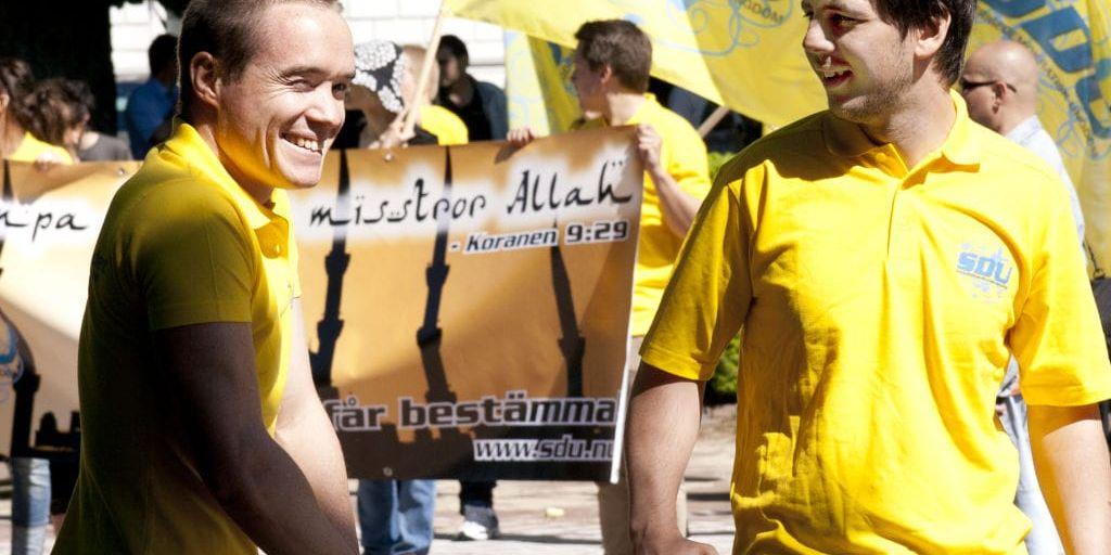 Gladlynt. 18 dagar efter rasistattacken i Stockholm är alla de tre Sverigedemokraterna och demonstrerar i Helsingborg. Då demonstrerade Kent Ekeroth mot ett påstått moskébygge tillsammans med Chang Frick. Båda var då anställda av partiet för att arbeta heltid för SD i valrörelsen 2010.